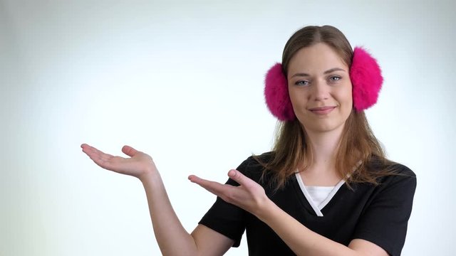 Young pretty girl in a black t-shirt and pink headphones pointing rightwards against white background. Cute smiling girl introduce product, pointing right blank copy space