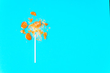 broken Lollipop on blue background with white plastic handle close up top view