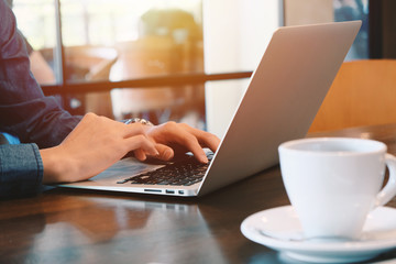 Close up of young businessman working remotely with computer laptop and coffee at home office during the spread of pandemic Covid-19 and Coronavirus, self quarantine and work from home