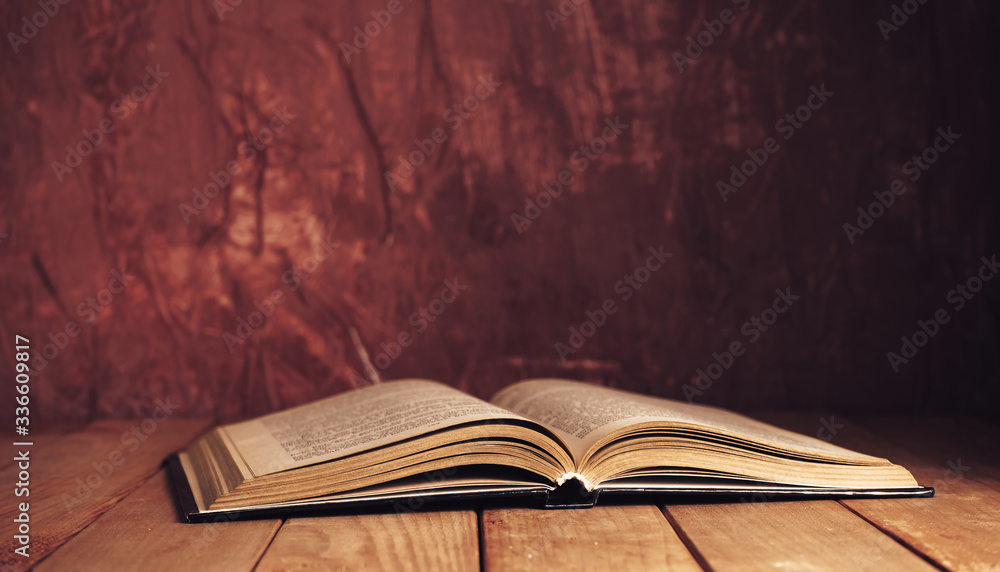 Aufkleber beautiful ancient open old book on a red wooden table and dark-red wall background behind.