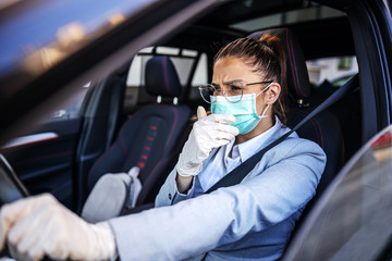 Fototapeta na wymiar Young woman with protective mask and gloves driving a car coughing. Infection prevention and control of epidemic. World pandemic. Stay safe.