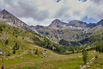 Naklejka premium View of a green lowland with small houses. In the background are high mountains and blue sky.