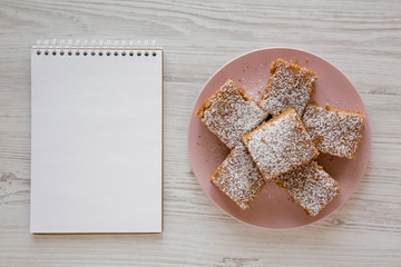 Homemade Tasty Applesauce Cake on a pink plate, blank notepad on a white wooden surface, top view. Flat lay, overhead, from above.