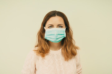 Portrait of a young woman wearing a protective medical face mask, looking at camera, close up, isolated on a light background. Influenza epidemic, dust allergy, corona virus protection. Selfisolation