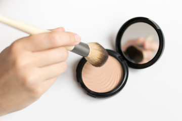 Hand holding a make up brush and highlighter with a little mirror