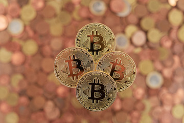 four bitcoin coins centered on top of many euro coins