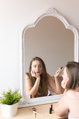 Young woman portrait putting on make up in front of a mirror