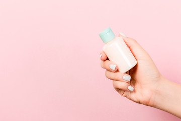 Pink background with female hand holding cosmetics bottle and copy space for your design