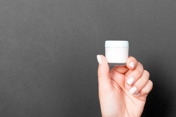 A jar of cosmetic product in a female hand at black background with copy space