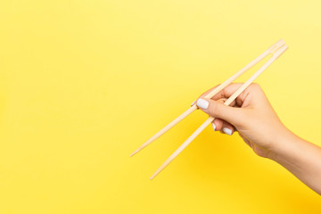 Girl's hand showing chopsticks on yellow background. Asian cuisine concept with empty space for your design