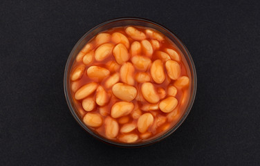 Baked beans in tomato sauce on black background, top view