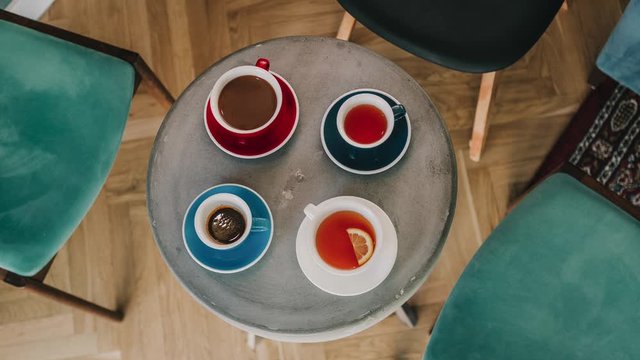 stop motion animation, cups with tea and coffee spin on a round concrete table, a female hand takes one of the cups 