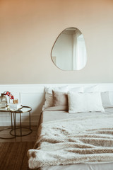 Stylish beige color bedroom with bed, linen, pillows, mirror, bedside table with red berries...