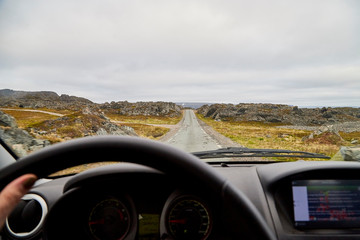 View from car window on the road and pity strange landscape with a mountains, rocks and cloudy sky and hand of woman. Landscape through windscreen in Norway
