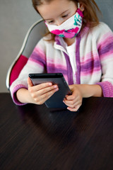 Young child girl at home, wearing a protection mask and gaming on a tablet, Coronavirus quarantine.