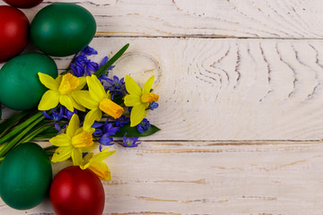 Painted Easter eggs and bouquet of yellow daffodils and blue scilla flowers on white wooden...