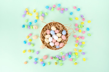 Top view of pot with shredded paper and colorful quail eggs placed on blue background during Easter celebration