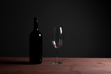 Black bottle of red wine and a glass. A bottle of wine stands on a table, a bottle on a gray background and a wooden table.