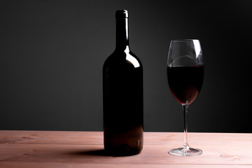 Black bottle of red wine and a glass. A bottle of wine stands on a table, a bottle on a gray background and a wooden table.