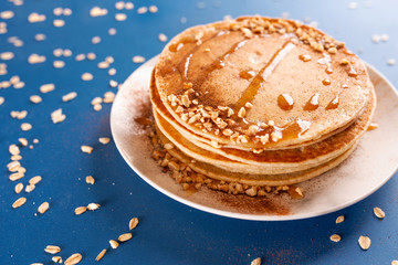 Oat pancakes on a white dish with nuts and syrup, with oatmeal.