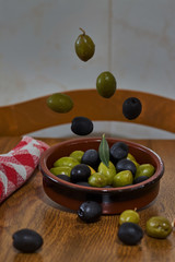 Green and black olives falling into a clay bowl