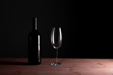 Black bottle of red wine and a glass. A bottle of wine stands on a table, a bottle on a gray background and a wooden table.