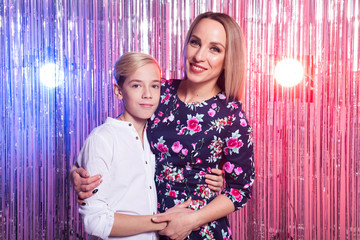 Mothers day, children and family concept - teen boy and his mom embracing on shiny party background.