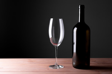 Black bottle of red wine and a glass. A bottle of wine stands on a table, a bottle on a gray background and a wooden table.