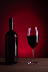 Black bottle of red wine and a glass. A bottle of wine stands on a table, a bottle on a gray background and a wooden table. Red vine.