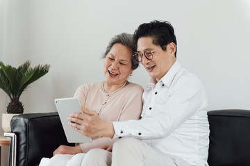 An elderly Asian couple using electronic devices on the sofa