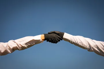 Foto op Plexiglas Handshake with black medical gloves, profile view on blue background. Covid-19 coronavirus ncov concept. © Inception