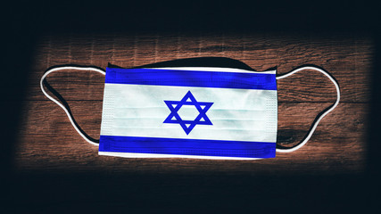 Israel National Flag at medical, surgical, protection mask on black wooden background. Coronavirus...
