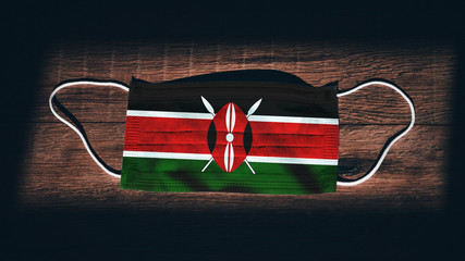 Kenya National Flag at medical, surgical, protection mask on black wooden background. Coronavirus...