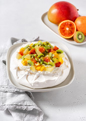 Tropical Pavlova meringue cake with kiwi, mango, pineapple, blood orange slices and whipped cream. Delicious summer dessert. Selective focus.