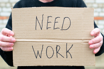 unemployed person holding a cardboard sign with a inscription need work