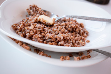 Buckwheat porridge with butter on a white plate with a spoon