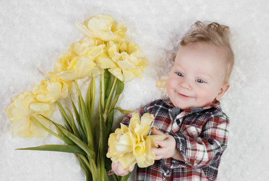 Cute little boy in a plaid shirt holds a bouquet of yellow tulips