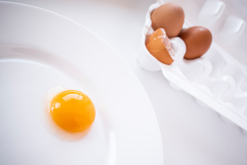 Egg yolk on a white plate. In the background there are two eggs in a package