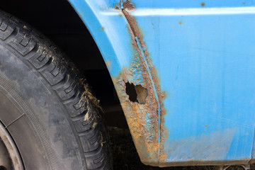The old battered car is blue, with traces of rust and damage. It is dangerous for drivers on the road.