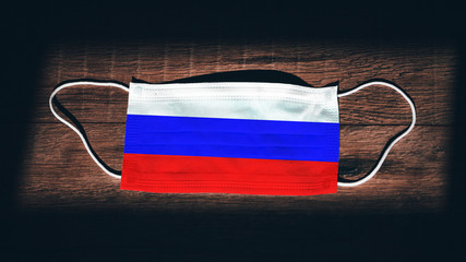 Russia National Flag at medical, surgical, protection mask on black wooden background. Coronavirus...