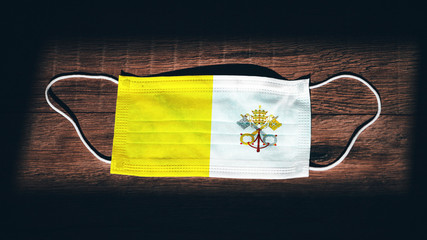 Vatican National Flag at medical, surgical, protection mask on black wooden background. Coronavirus...