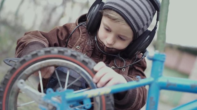 A boy of 5 years old in acoustic headphones of the 80s era, diligently maintains his children's bicycle.