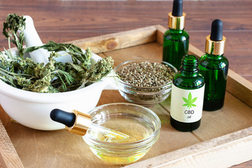 Bottles of hemp oil with cannabis seeds and dry leaves on white wooden table. Alternative medicine concept.
