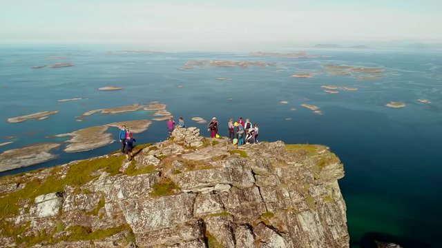 4K drone aerial shot with orbit motion of happy climbers on the top of the mountain. Panorama view of sunset in Northern Norway.