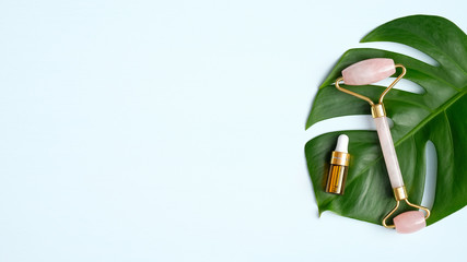 Rose quartz facial massage roller with essential oil on monstera leaf. Face massage tool,...