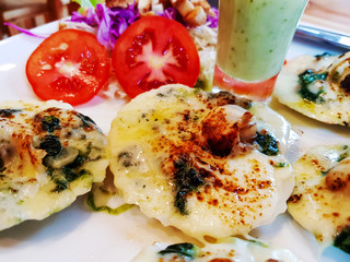 Baked scallops, cheese and spinach with dipping sauce on a white plate at the restaurant