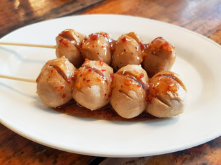 Grilled skewer beef ball with flavored sauce placed on a plate.