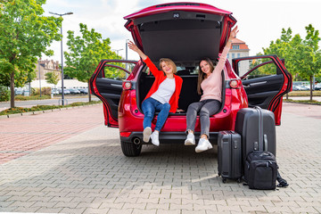 Two girls chat while sitting in open trunk of car