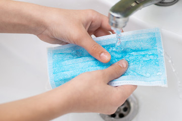 Hands of child washing her disposal mask in the sink in the bathroom. Concept of lack of protective...
