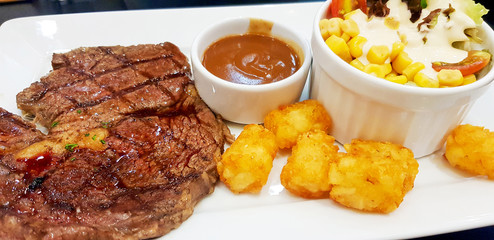 Beefsteak with side dishes consisting of fried potatoes, salad and tomato sauce